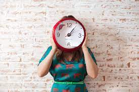 Person holding red clock in front of their face. 