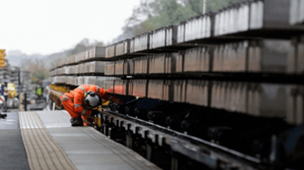 A Network Rail engineer peering under machinery from a station platform