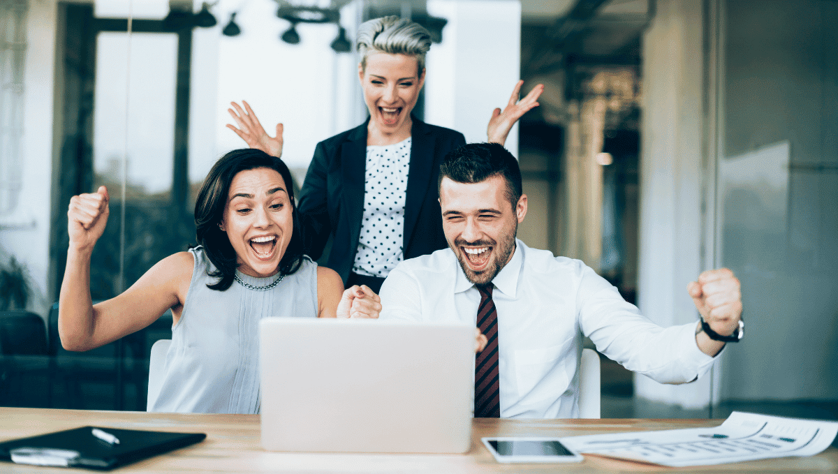 Three people in an office celebrating with hands up and fists clenched in a 'yes' gesture.