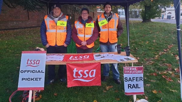 3 TSSA pickets, 1 man, 1 woman, 1 younger man, behind a pasting table with TSSA picket posters in front