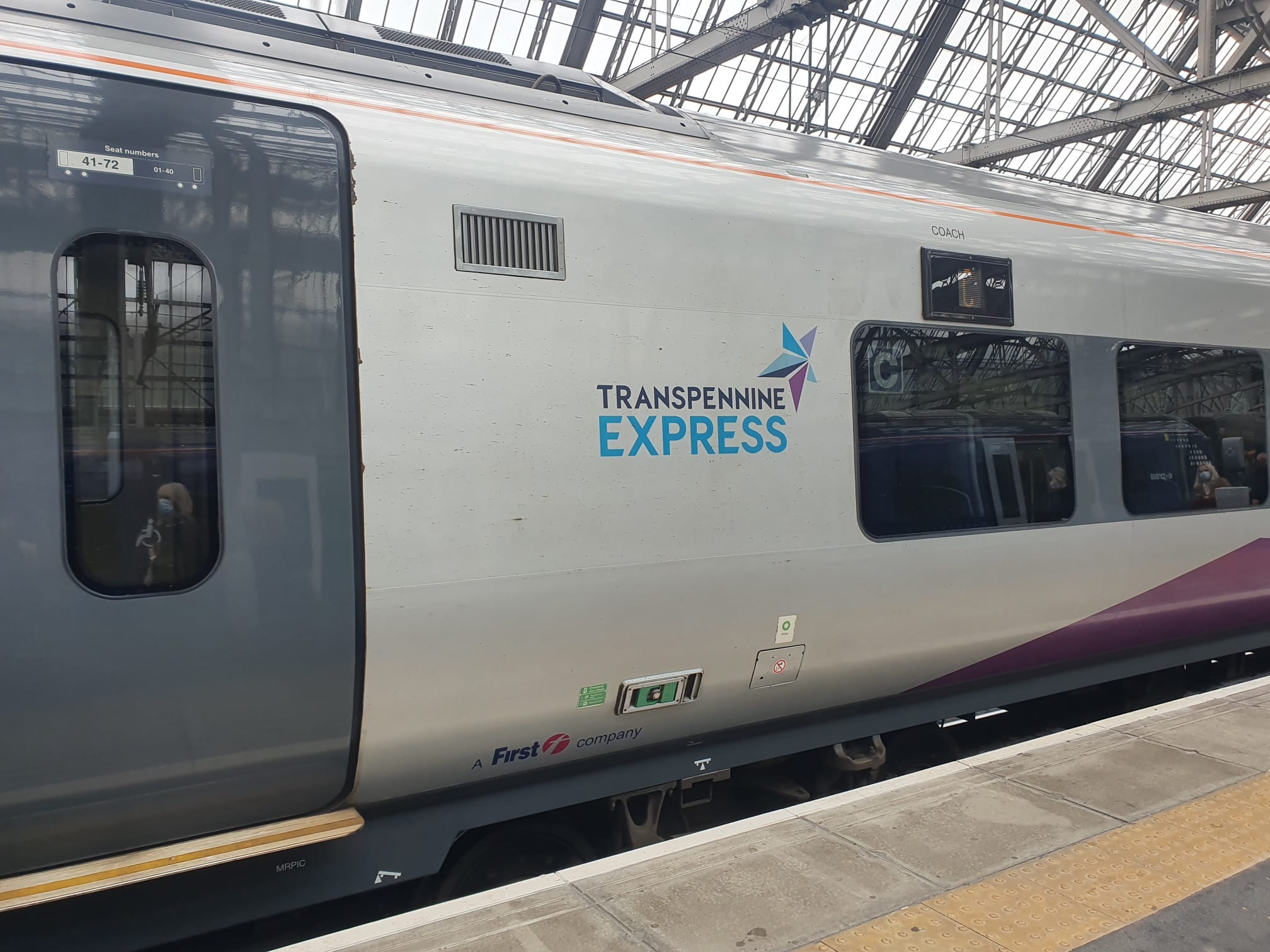 A train carriage in Transpennine Express livery with text reading "Transpennine Express" and a blue and purple star on the side. 