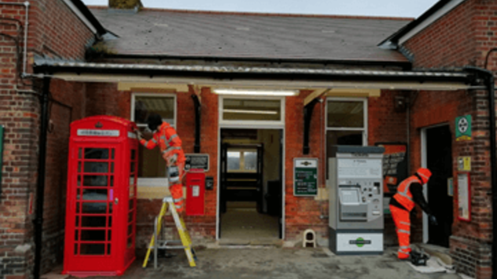 Network Rail workers in high vis working on station refurbishment with red phone box and ticket machine in shot