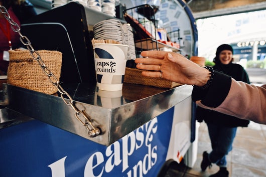 A hand reaching for a coffee at the Leaps & Grounds coffee cart