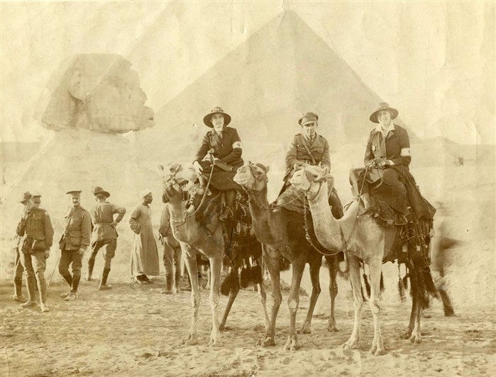 Ms M. Millbanke on camel with others in front of Pyramids in Cairo, Egypt.