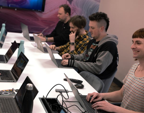 Four 26 employees sat around a table, looking at their laptops. The person in the foreground is smiling.