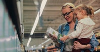 A person standing in a supermarket aisle and holding a child in their arms. Both are looking and holding at Arla Foods carton of milk.
