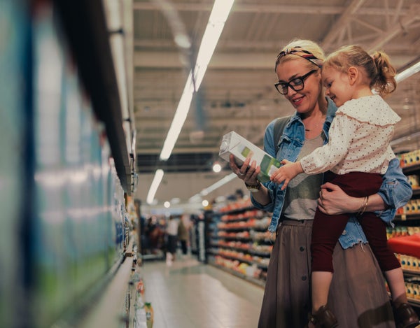 A person standing in a supermarket aisle and holding a child in their arms. Both are looking and holding at Arla Foods carton of milk.