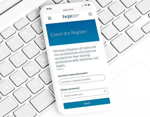 A smart phone on a computer keyboard, the phone screen shows the HCPC registration site.