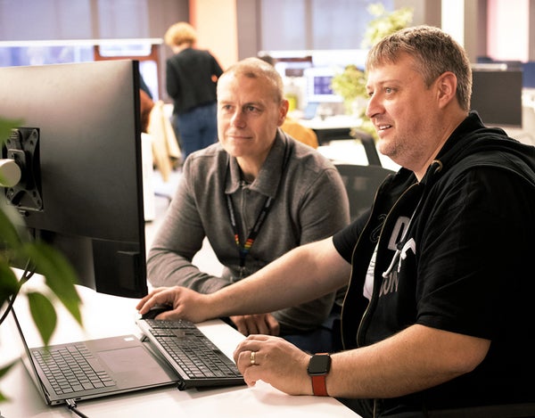 Two 26 employees sat at a desk and looking at a computer screen.