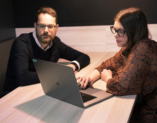 Two 26 employees sat at a desk and looking at a computer screen.
