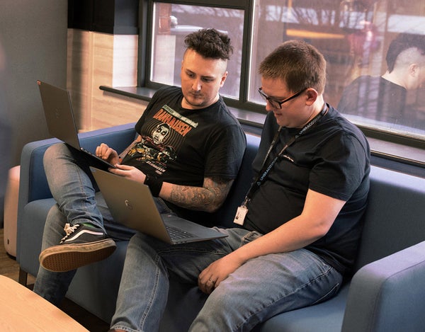 Two 26 employees sat on a sofa and looking at one of their laptops.