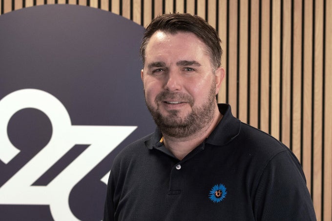 Headshot of Guy Hunsworth, with the 26 logo in the background.