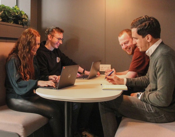 Four 26 employees sat around a table, with laptops and a notebook.