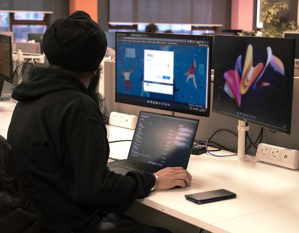 A person sat at their computer desk and looking at one of their computer's two extra monitors. There is also a laptop on the desk.