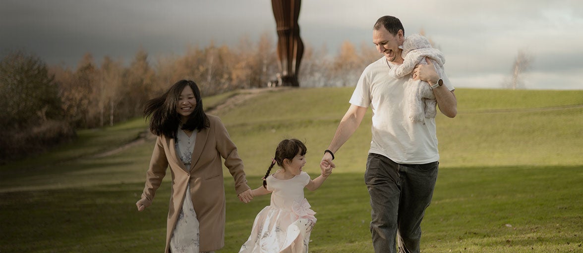 A young family of four walking down a field laughing and smiling with one another. 