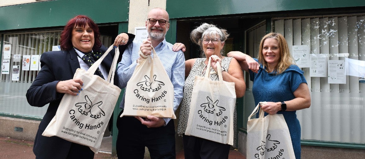 Four people with Caring Hands tote bags.