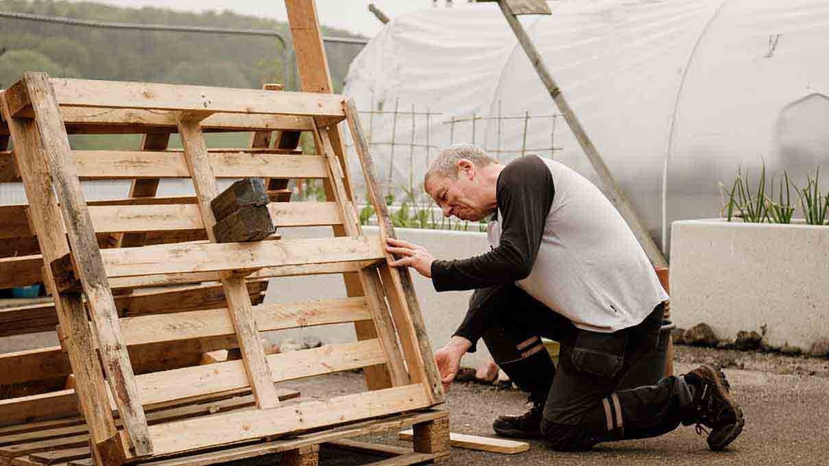 Man kneeling on the floor holding a wooden palette. 