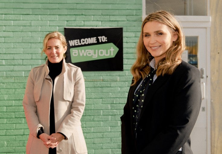 Two women in front of the 'welcome to a way out' sign.