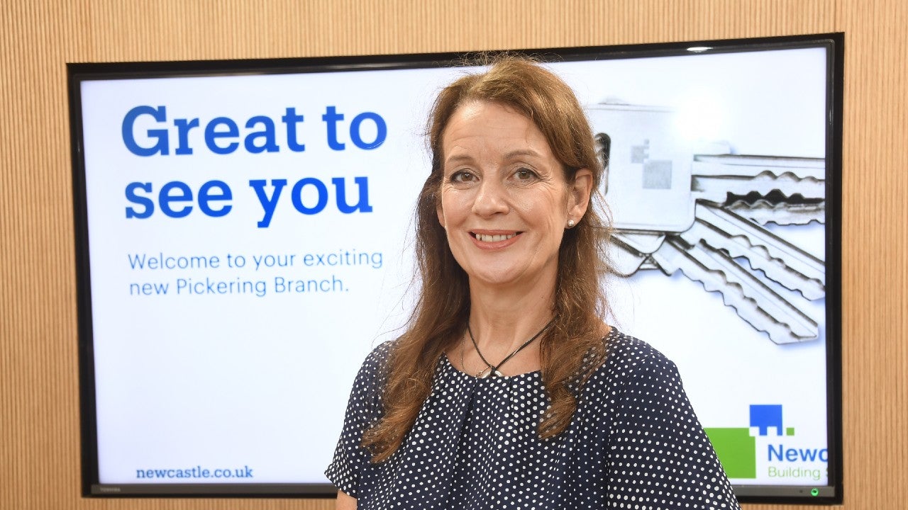 Newcastle Building Society's Pickering Branch Manager, Vanessa, stood smiling in front of a screen that reads: "Great to see you. Welcome to your exciting new Pickering Branch."