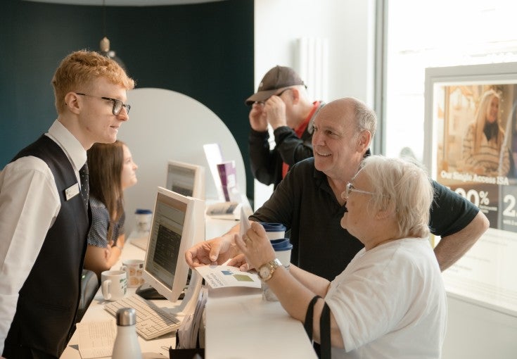 A Newcastle Building Society Customer Adviser speaking to two members at the branch counter.