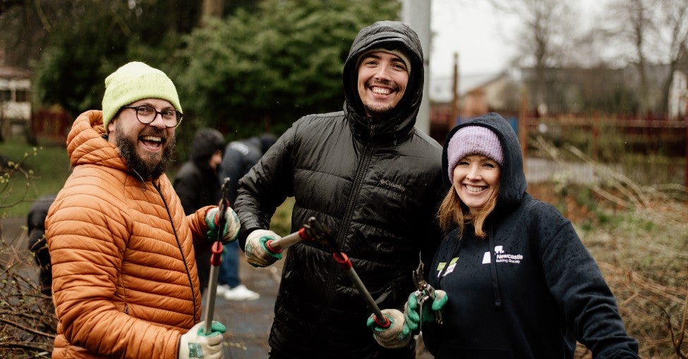 Three colleagues smiling at the camera holding garden shears, doing some volunteering at Wallsend Park.