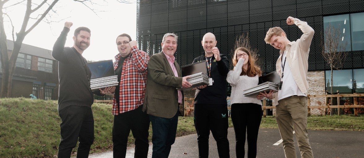 Newcastle Building Society colleagues and members of Newcastle United Foundation's employability programme stood outside of the Foundation's community facility, holding laptops and punching one arm up in the air in celebration.