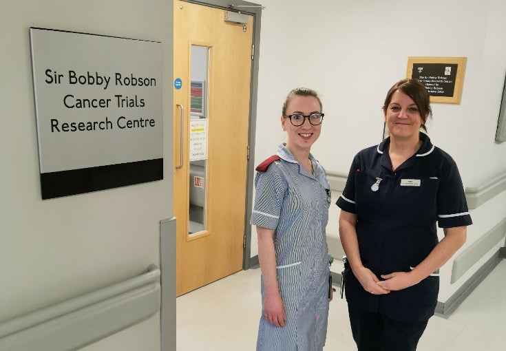 Two NHS staff members stood outside of the doors to the Sir Bobby Robson Cancer Trials Research Centre.