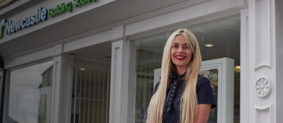 Area Manager, Sarah, stood in front of a Newcastle Building Society branch, smiling. 