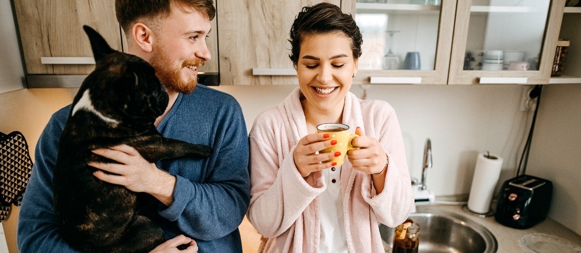 A couple stood in their kitchen with their dog and a cup of coffee