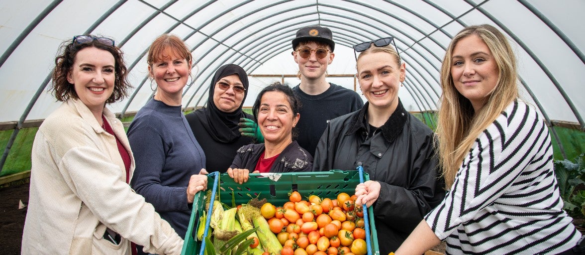 A group of Newcastle Building Society colleagues and members of West End Women and Girls Centre stood holding a basket of vegetables. The vegetables have been grown by members of the charity on their farm.