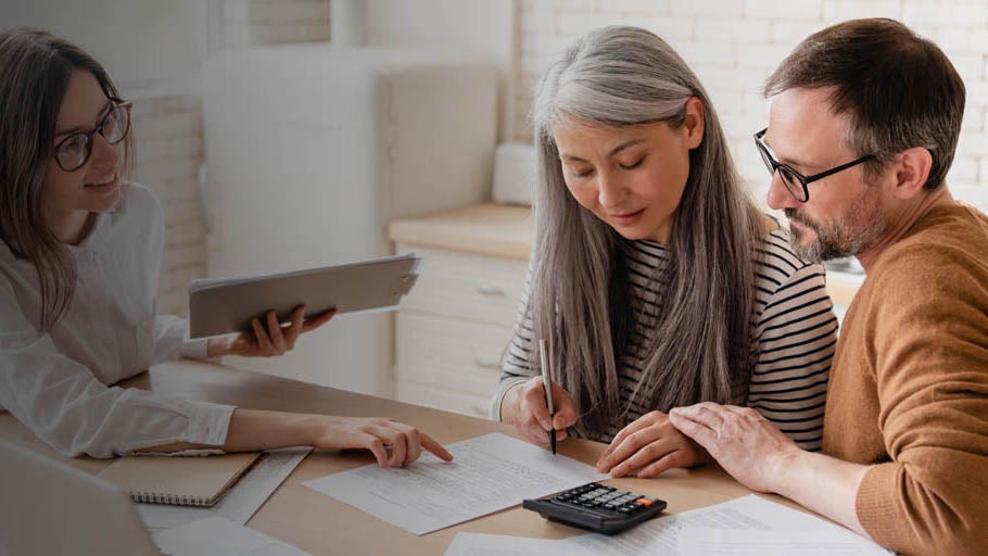 Man and woman sat with their financial adviser, going through paperwork.