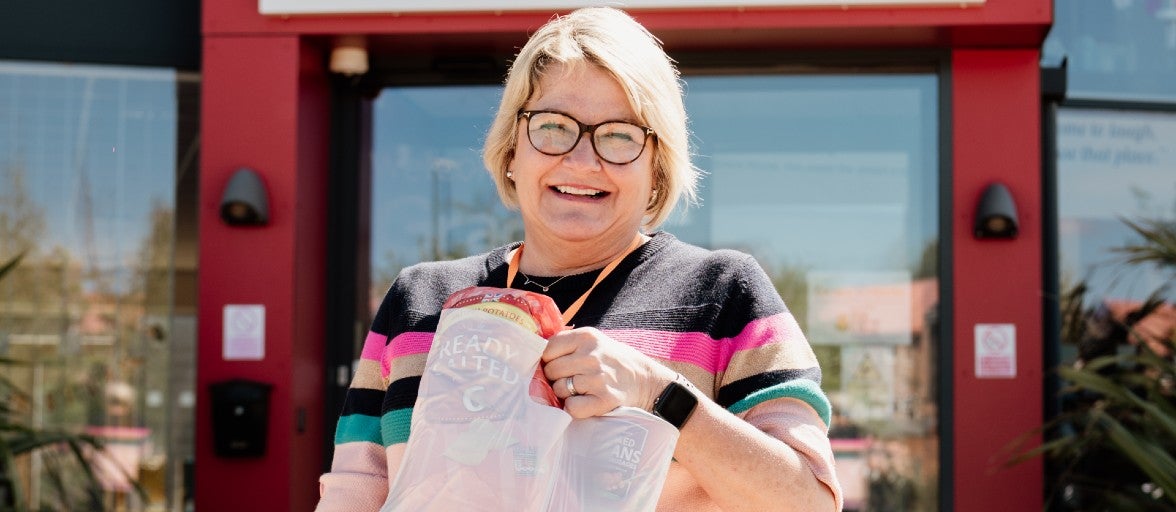 A lady stood outside of Grace House in Sunderland, holding a shopping bag full of food and smiling at the camera.