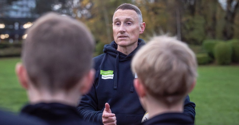 A close up of a man talking to two schoolchildren he coaches rugby.