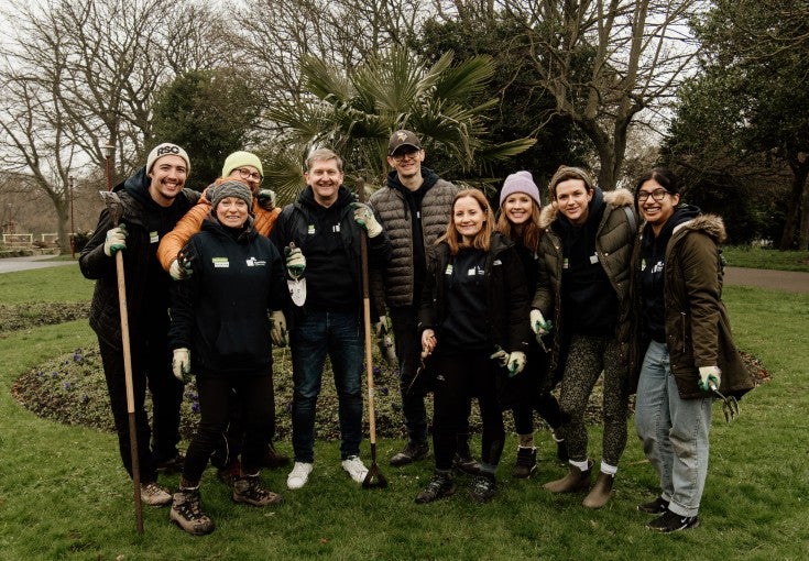 Group of Newcastle Building Society colleagues stood in Wallsend park with gardening tools in hand smiling.