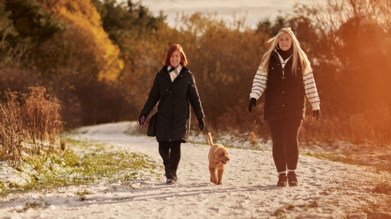 Two women walking a dog in a snowy park.