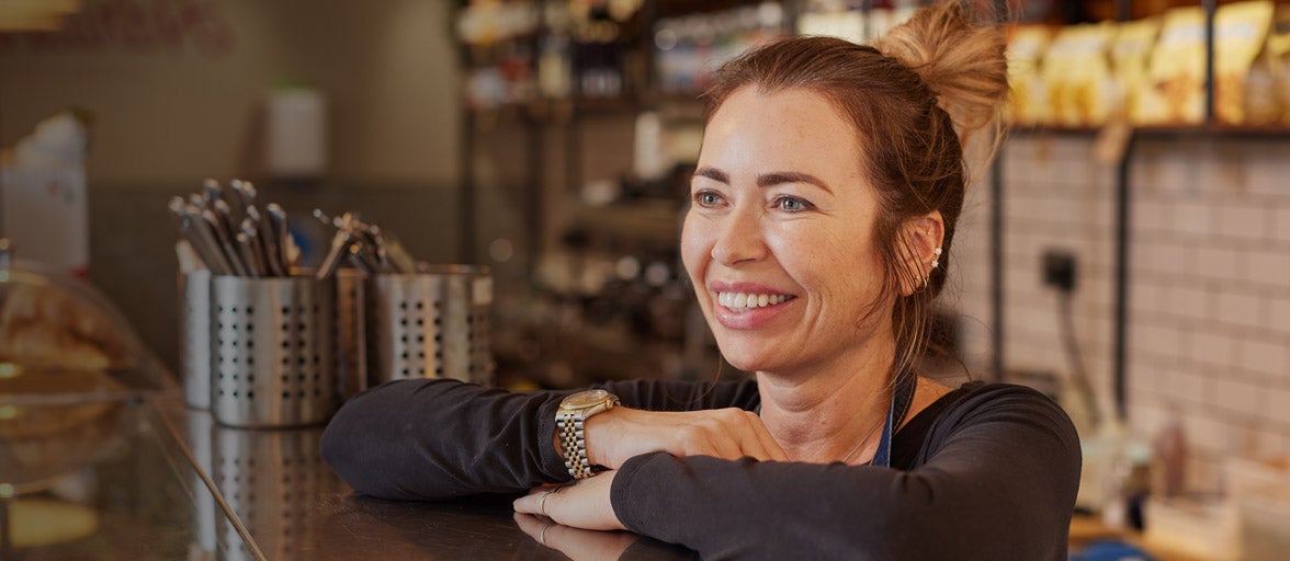 Lady stood at a deli counter smiling 