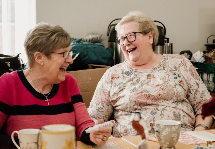 Two elderly ladies laughing with each other as they play bingo.