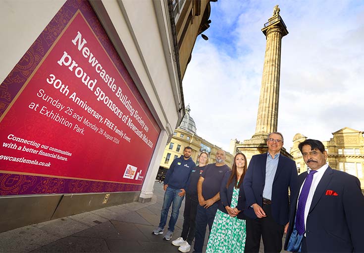 six people standing in front of Grey's Monument in Newcastle by the Newcastle Building Society branch window with a Newcastle Mela hoarding 