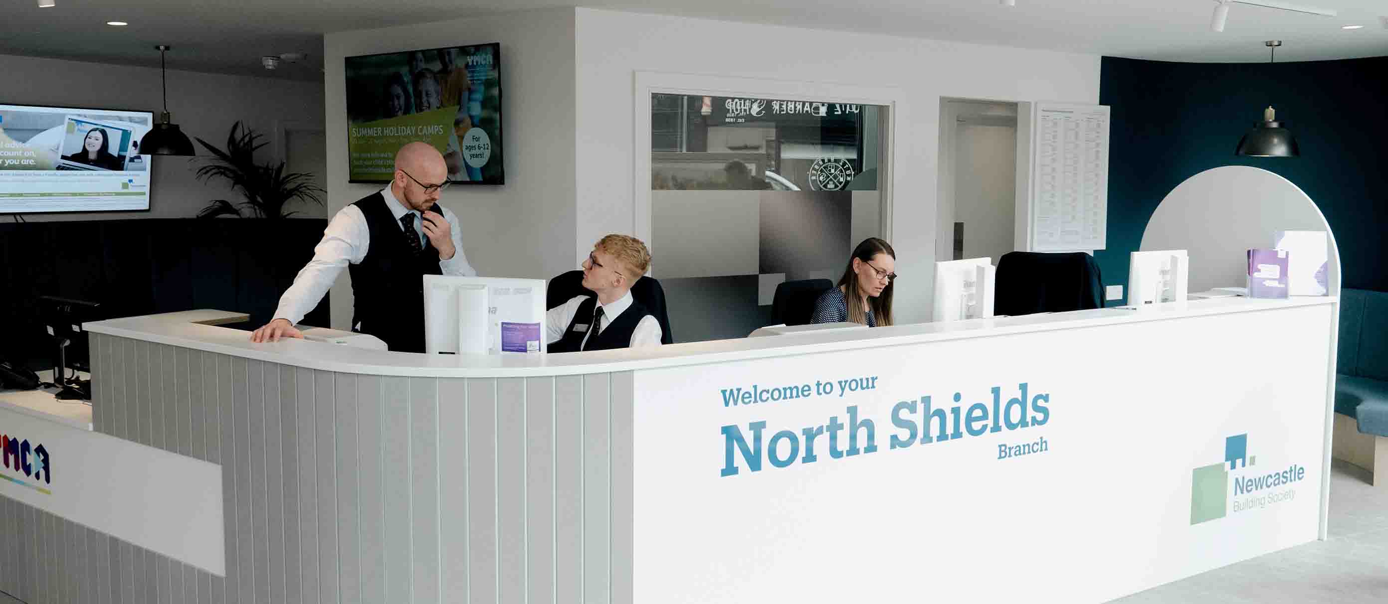 Interior image of North Shields community branch, with three Newcastle Building Society colleagues working bedhing the front desk. 