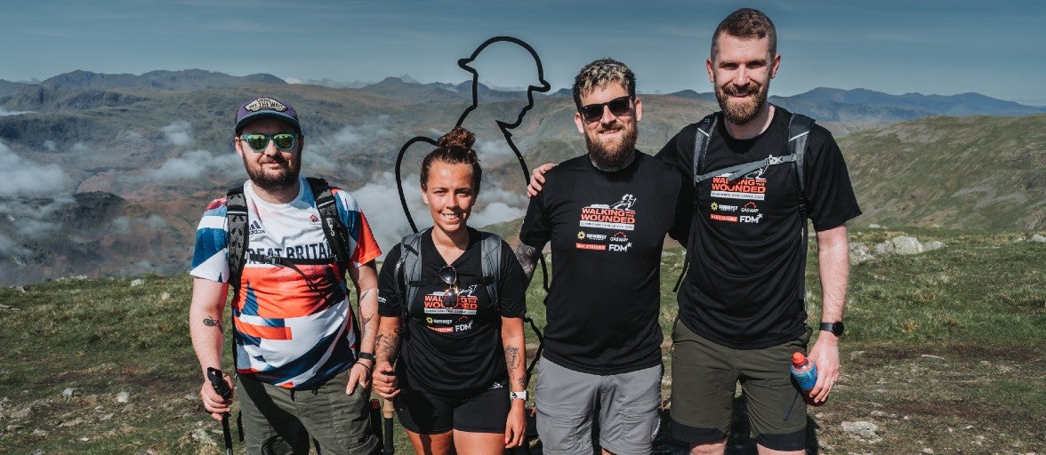 Four IT colleagues stood at the top of a fell during Walking With The Wounded's Cumbrian Challenge, facing the camera and smiling.