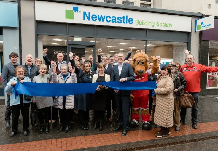 A group of colleagues, customers, and customers of Newcastle Building Society, preparing for a ribbon cutting to launch the new Middlesbrough branch.