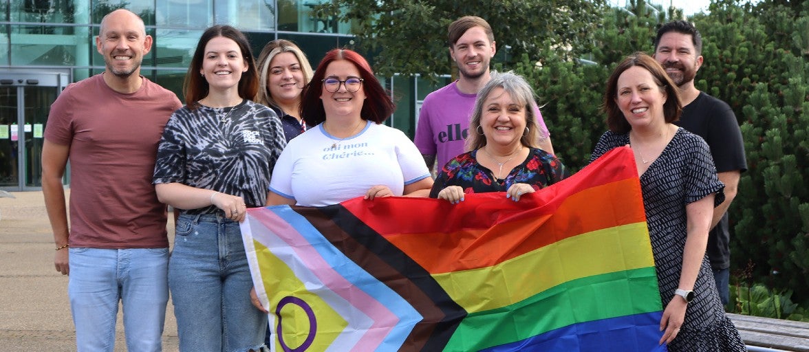 A group of colleagues stood outside an office holding a Pride flag. 