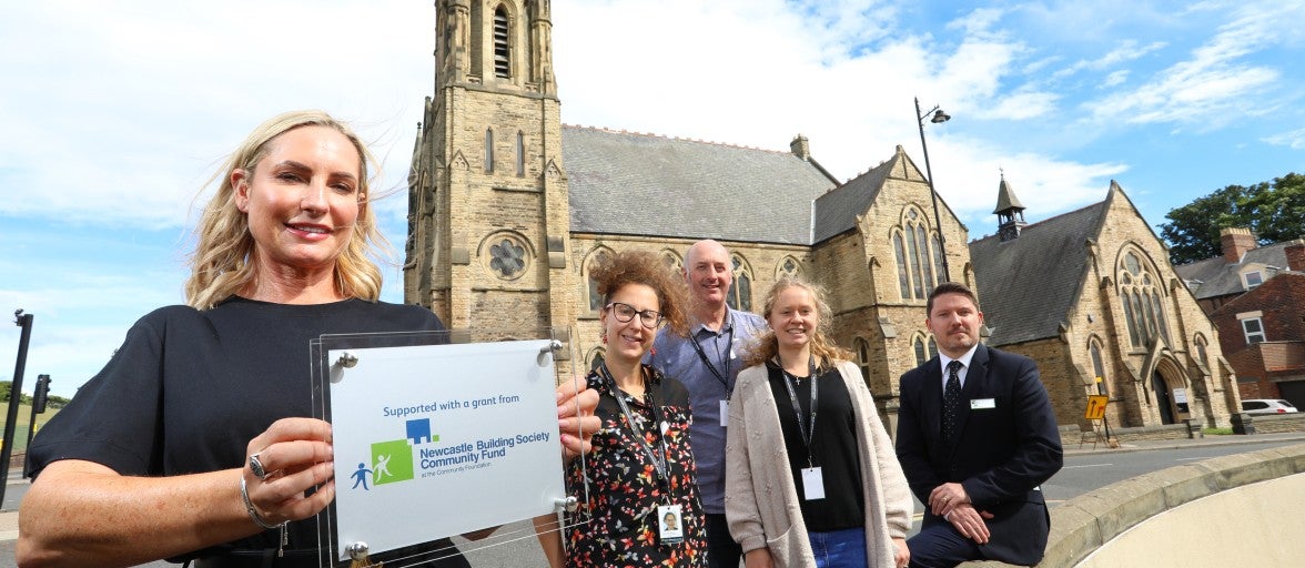 A group of people outside a church in Sunderland with a community grant plaque