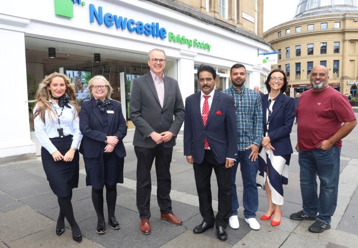 A group of people standing in front of the Newcastle Building Society Monument branch.