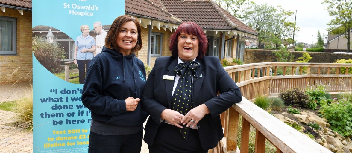 Two ladies smiling next to a St Oswald's Hospice sign.