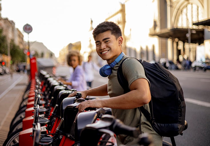 A young man exploring the city, renting an electric bicycle and smiling.