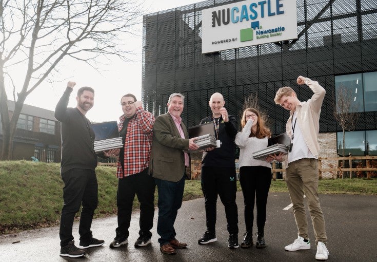 Newcastle Building Society colleagues and members of Newcastle United Foundation's employability programme stood outside of the Foundation's community facility, holding laptops and punching one arm up in the air in celebration.