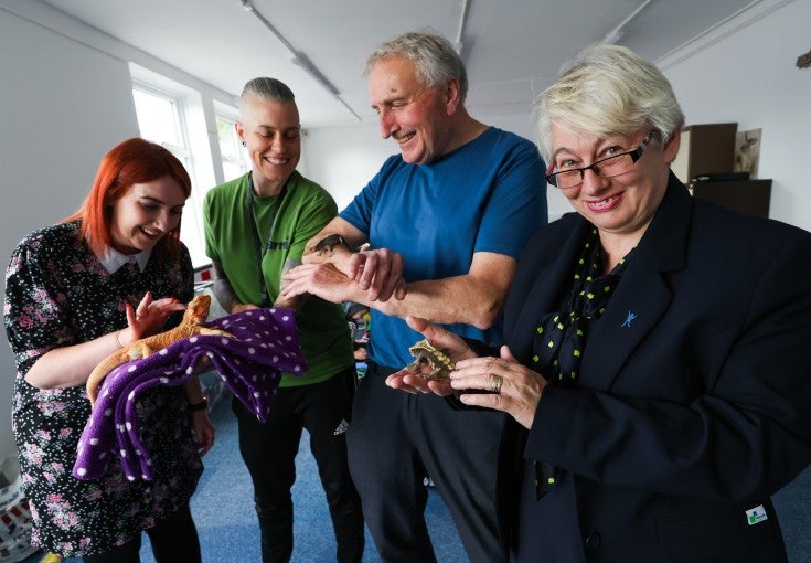 A group of four people holding some animals, including a bearded dragon and a frog.