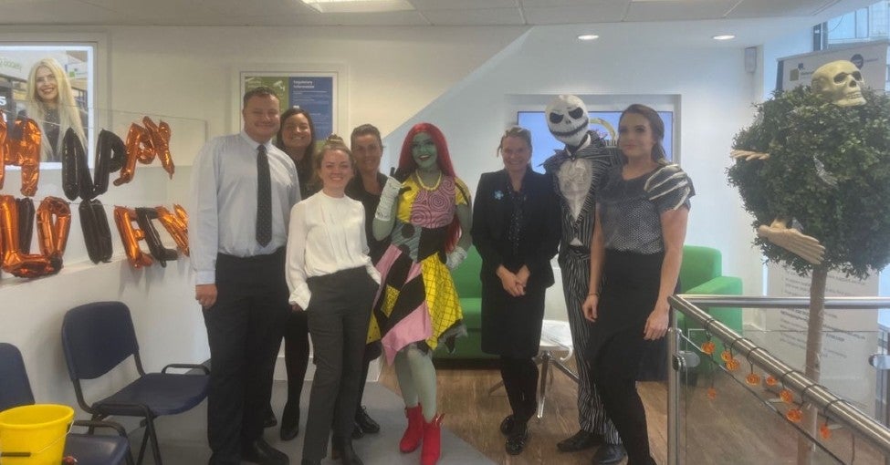 A group of building society staff posing with Jack and Sally, from the film 'Nightmare Before Christmas', and surrounded by Halloween decorations. 