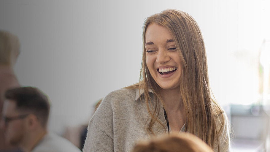 A woman laughing wearing a grey jumper.